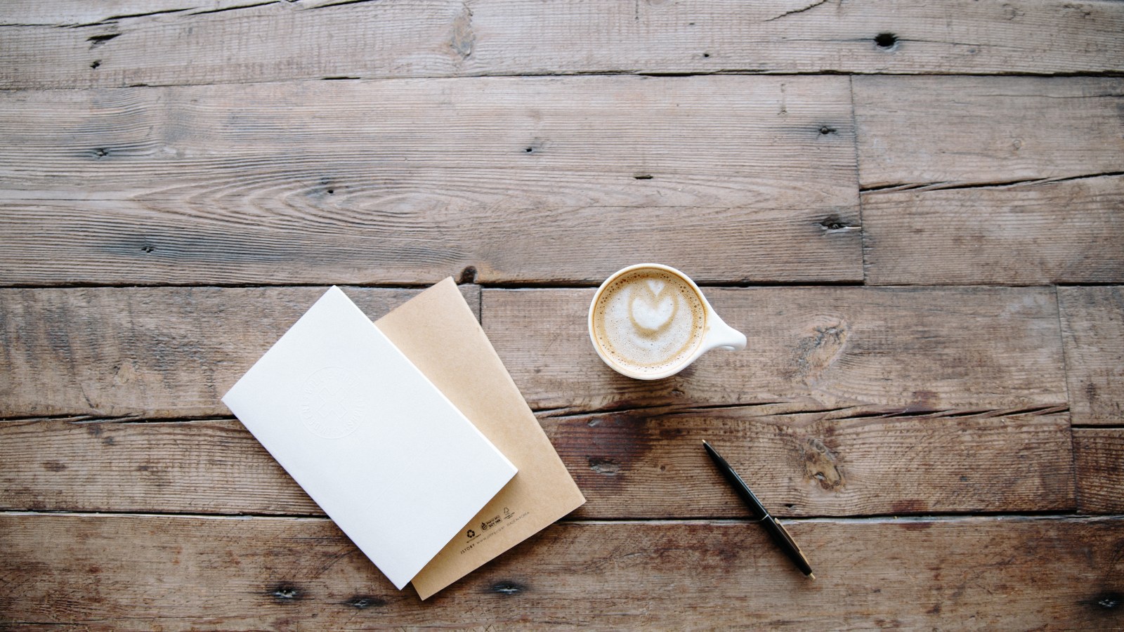 Taccuini, una penna e un caffe su un piano di lavoro.